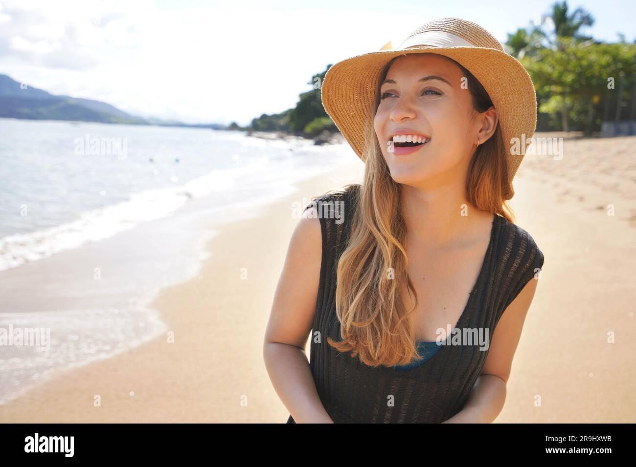 Primo piano di una bella giovane donna che indossa abiti estivi e cappello di paglia sulla spiaggia tropicale Foto Stock