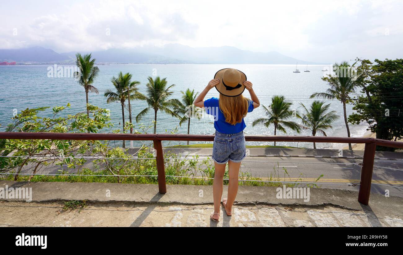 Vacanze a Ilhabela, Brasile. Vista panoramica della ragazza viaggiatrice con cappello che si gode la vista dal belvedere Morro da Cruz, dall'isola di Ilhabela, Brasile. Foto Stock