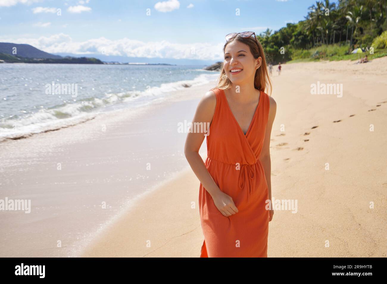 Bellissima giovane donna con un abito da sole arancione e occhiali da sole in testa nella destinazione estiva dell'isola di Ilhabela, Brasile Foto Stock