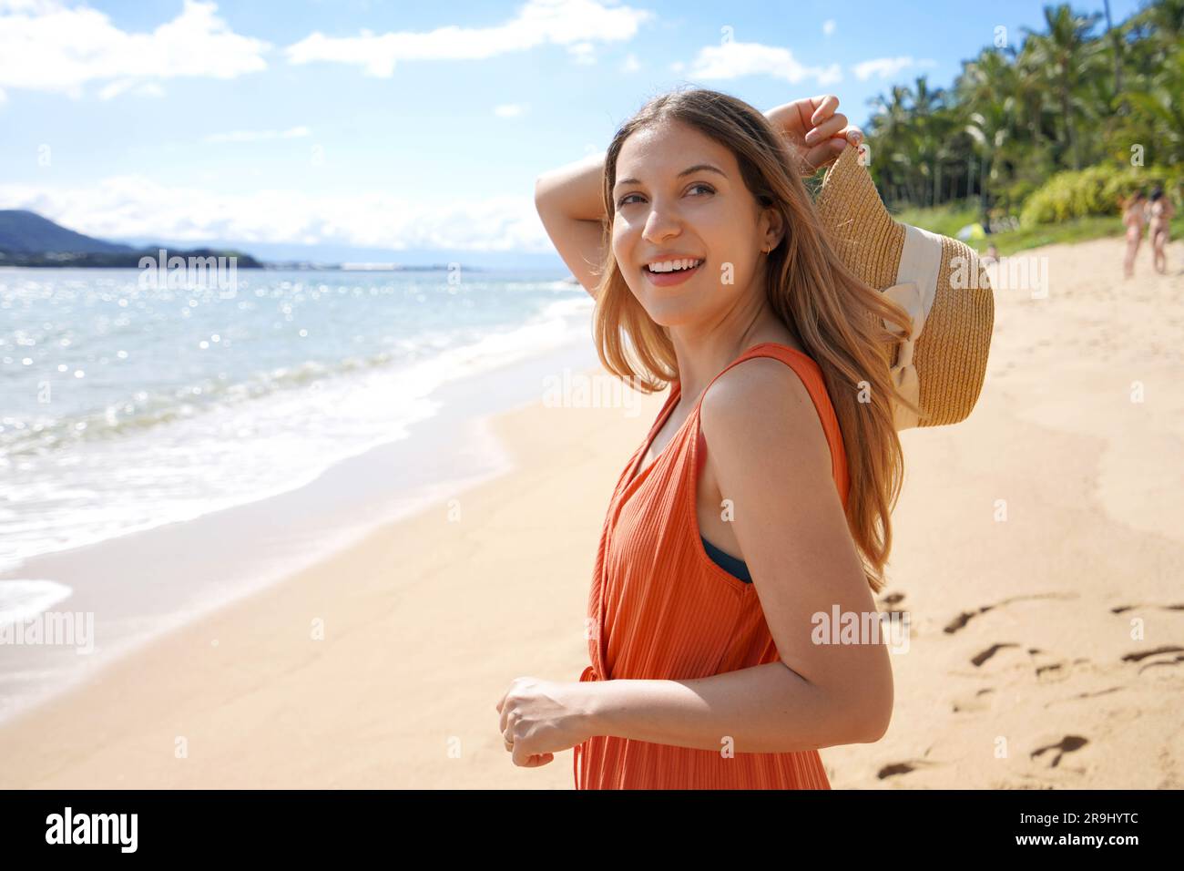 Ritratto di una bella ragazza spensierata che regge un cappello di paglia sulla spiaggia tropicale che guarda lontano Foto Stock