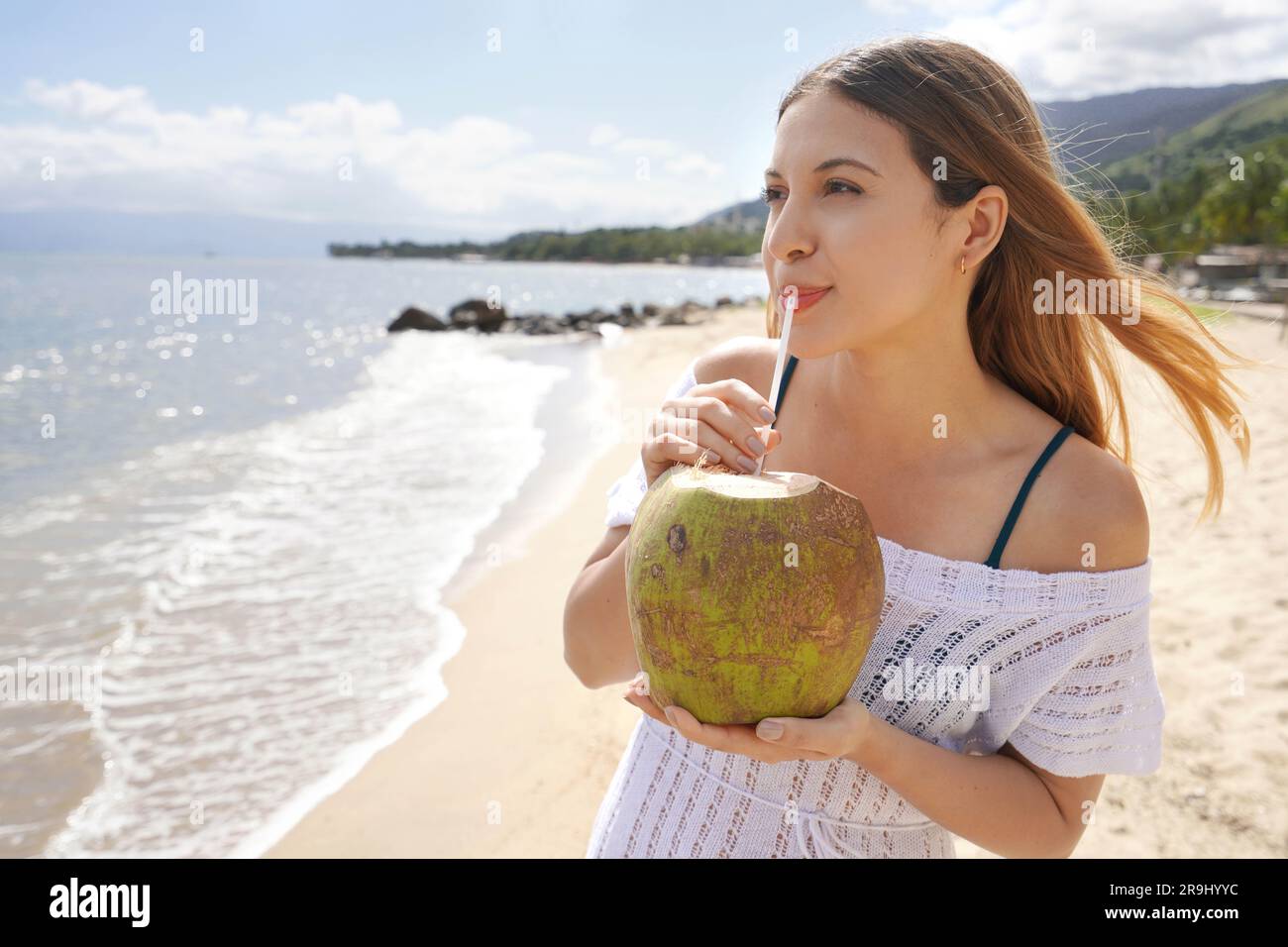 Ragazza brasiliana che beve acqua di cocco fresca sulla spiaggia. Concezione rinfrescante e naturale di cocco verde. Foto Stock