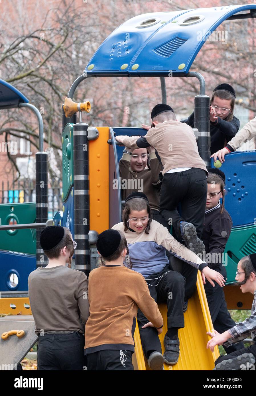 Giocosi bambini ebrei ortodossi giocano su uno stagno scorrevole durante la pausa nella loro yeshiva. A Brooklyn, New York, autunno 2022. Foto Stock