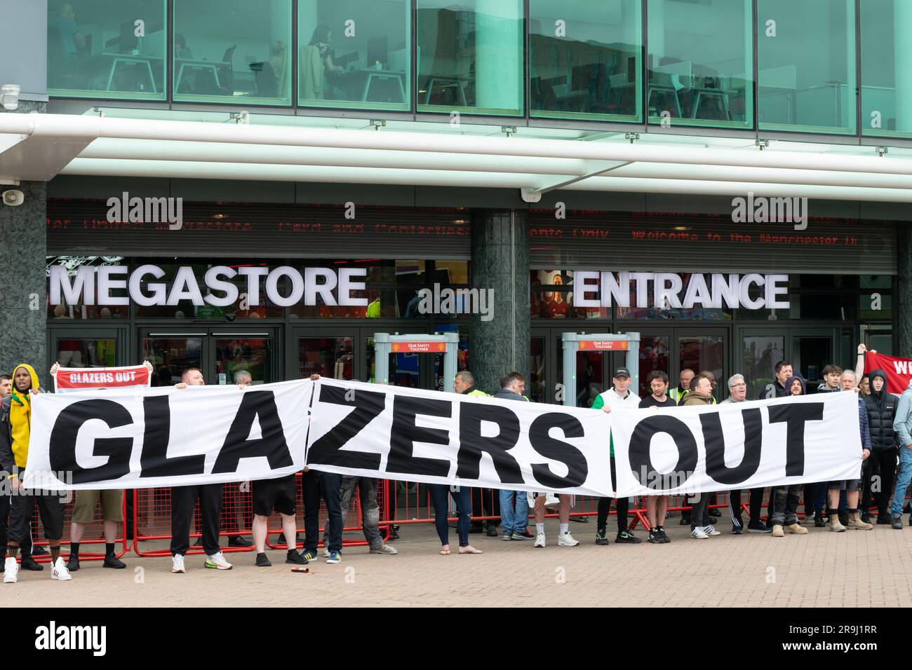 I manifestanti fuori dal campo di calcio del Manchester United chiudono il megastore il giorno in cui il club svela la loro nuova maglia di casa. Striscione testo Glazers Out. Foto Stock