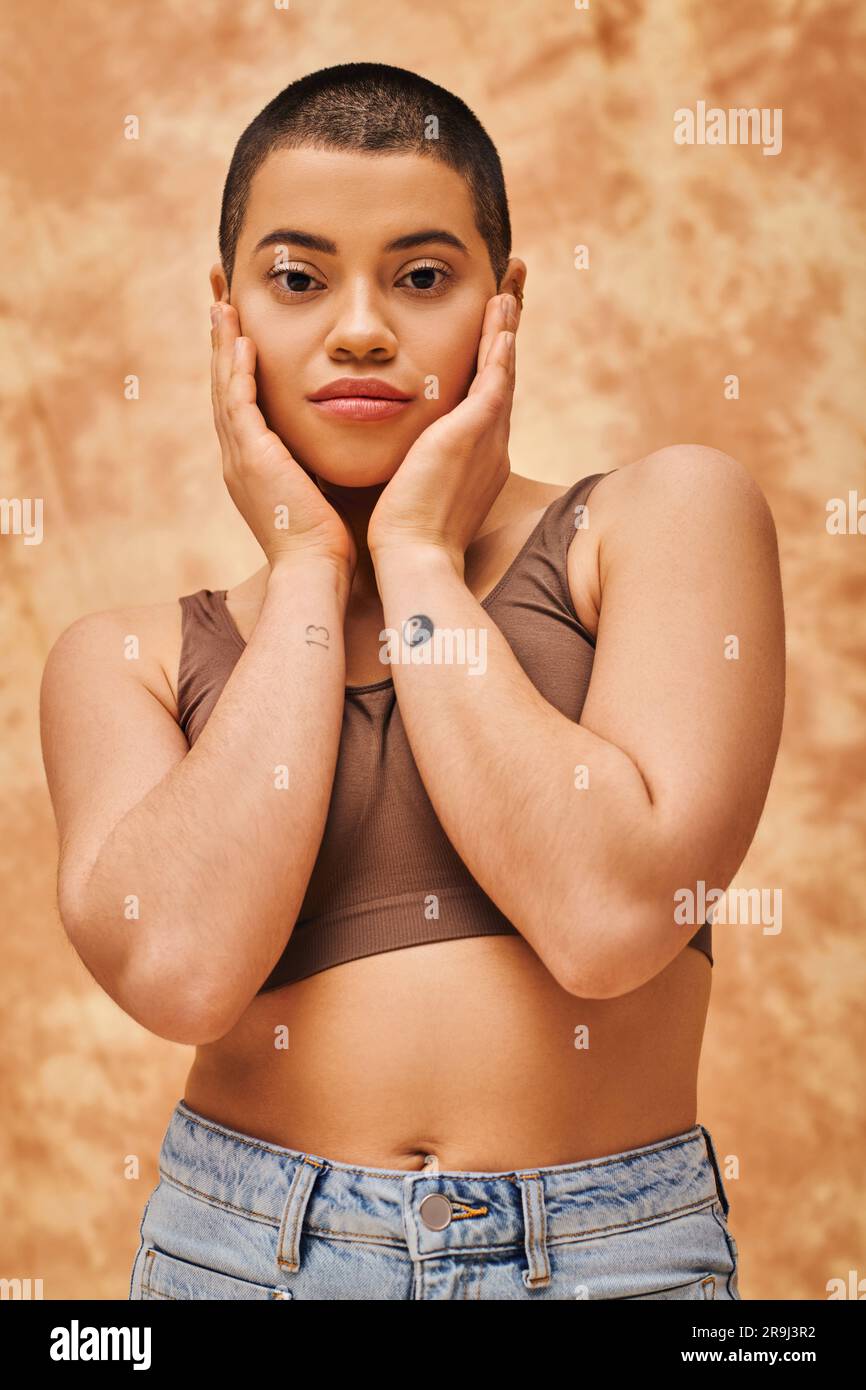 positività e sicurezza del corpo, giovane donna curvy in top in posa su sfondo beige macchiato, pelo corto, auto-accettazione, generazione z, tatuaggio Foto Stock