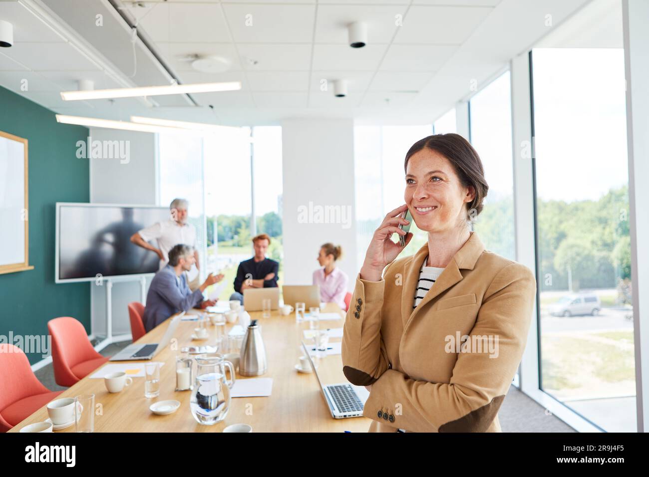 Donna d'affari felice che parla con uno smartphone con il team sul posto di lavoro Foto Stock