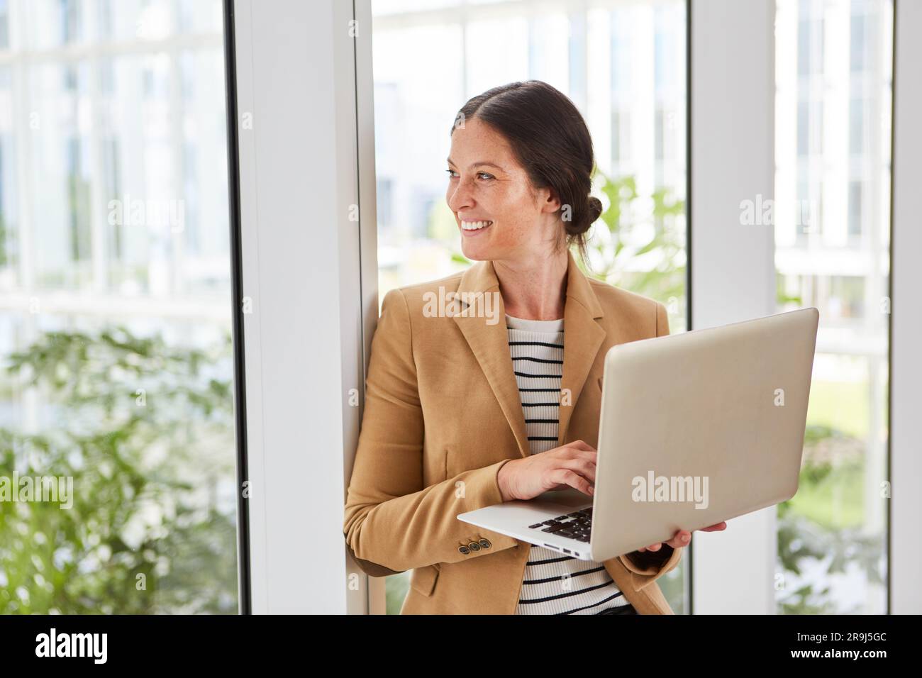 Felice donna d'affari che tiene un giorno in cui sogna un computer portatile nella sala Foto Stock
