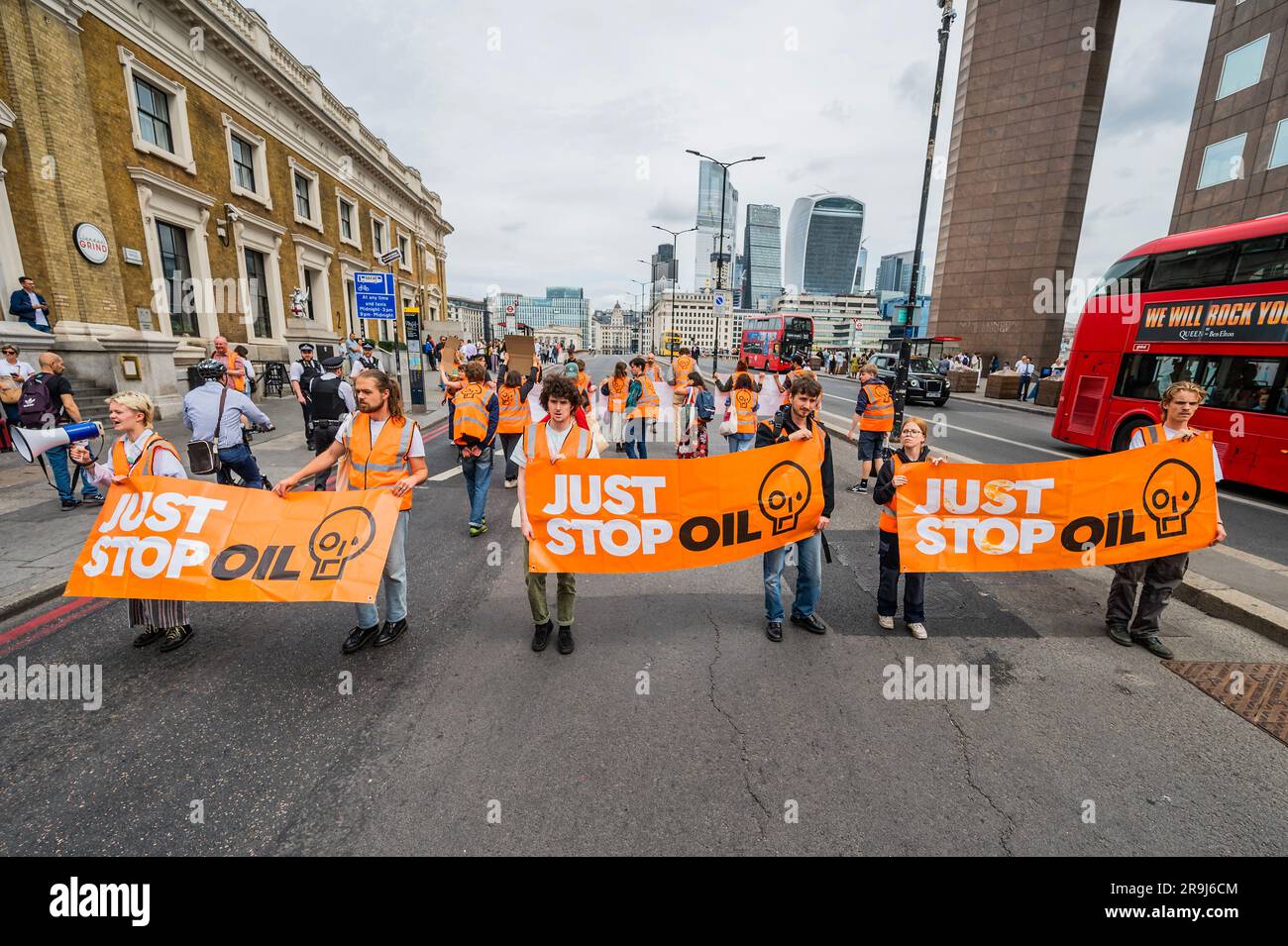 Londra, Regno Unito. 27 giugno 2023. La polizia inizia immediatamente ad avvertire la protesta che stanno bloccando la strada e causando e offendere ai sensi della sezione 12 del Public Order Act, ma lasciano passare autobus e biciclette - basta fermare la protesta petrolifera al London Bridge. L'obiettivo generale del gruppo è quello di convincere il governo a fermare tutti i nuovi giacimenti petroliferi nell'ambito degli sforzi volti ad evitare la crisi climatica. Crediti: Guy Bell/Alamy Live News Foto Stock