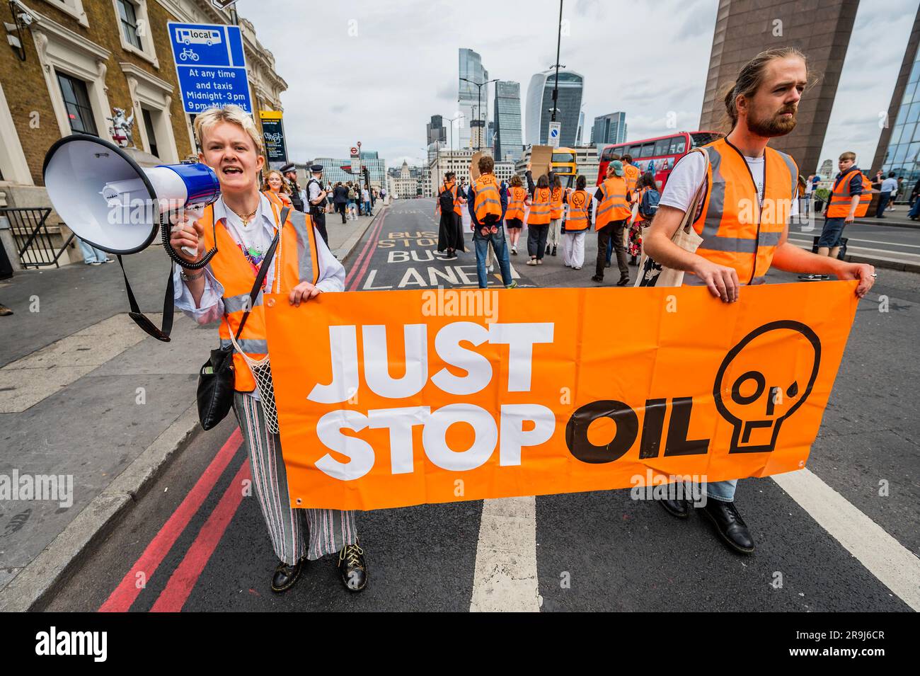 Londra, Regno Unito. 27 giugno 2023. La polizia inizia immediatamente ad avvertire la protesta che stanno bloccando la strada e causando e offendere ai sensi della sezione 12 del Public Order Act, ma lasciano passare autobus e biciclette - basta fermare la protesta petrolifera al London Bridge. L'obiettivo generale del gruppo è quello di convincere il governo a fermare tutti i nuovi giacimenti petroliferi nell'ambito degli sforzi volti ad evitare la crisi climatica. Crediti: Guy Bell/Alamy Live News Foto Stock
