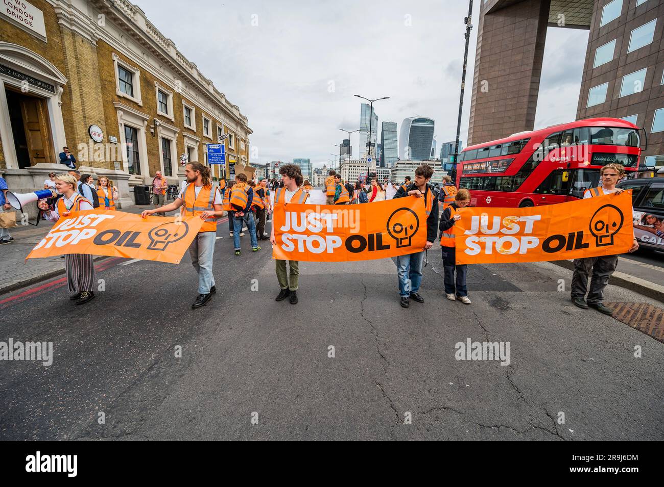 Londra, Regno Unito. 27 giugno 2023. La polizia inizia immediatamente ad avvertire la protesta che stanno bloccando la strada e causando e offendere ai sensi della sezione 12 del Public Order Act, ma lasciano passare autobus e biciclette - basta fermare la protesta petrolifera al London Bridge. L'obiettivo generale del gruppo è quello di convincere il governo a fermare tutti i nuovi giacimenti petroliferi nell'ambito degli sforzi volti ad evitare la crisi climatica. Crediti: Guy Bell/Alamy Live News Foto Stock