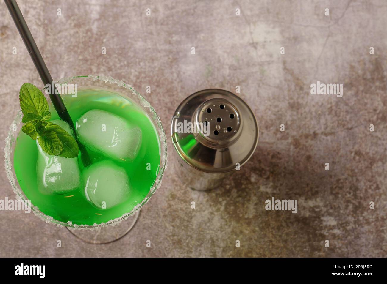 vista dall'alto di un cocktail verde con ghiaccio alla menta e paglia i bordi del bicchiere hanno zucchero a velo e uno shaker per accompagnarlo Foto Stock