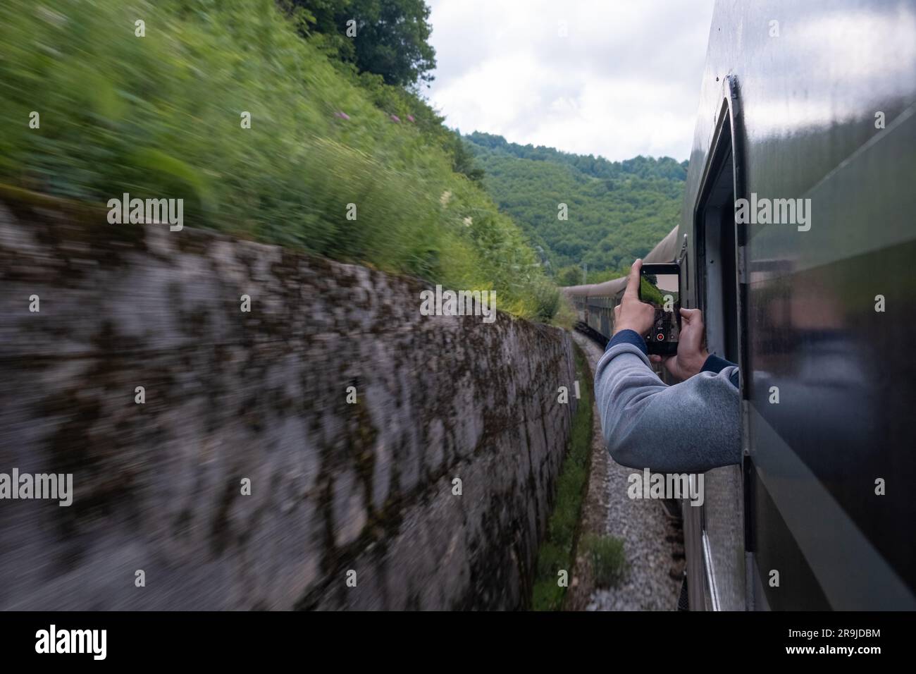 Uomo viaggiatore che fotografa la ferrovia dalla finestra del treno usando la fotocamera sul suo cellulare mentre viaggia in treno attraverso i Balcani Foto Stock