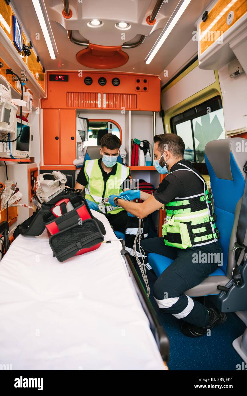 Gli operai dell'ambulanza indossano uniformi e maschere mediche con guanti seduti in automobile moderna durante il giorno lavorativo Foto Stock