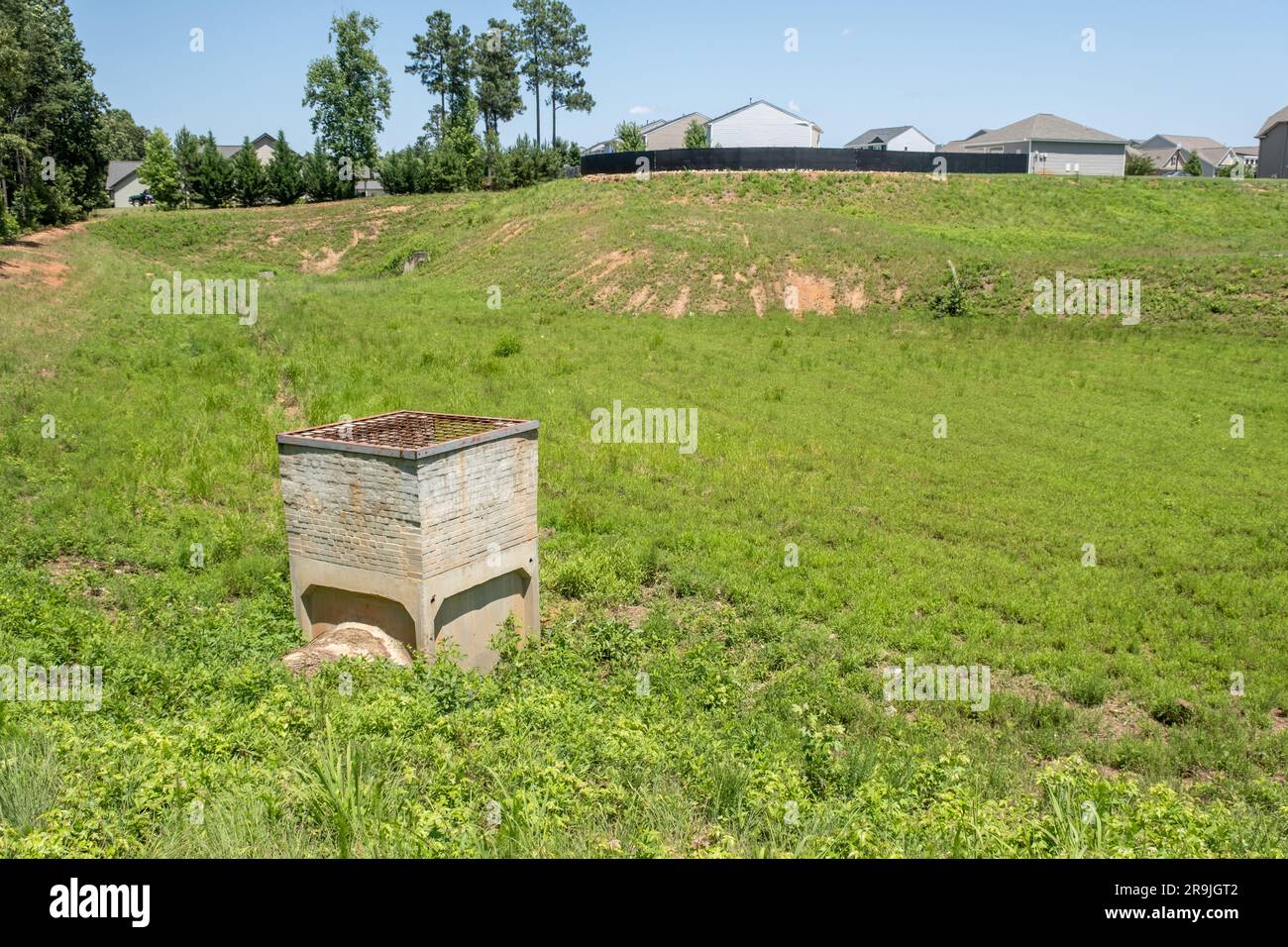 Grande fosso di drenaggio rivestito di erba e erbacce dietro una suddivisione Foto Stock