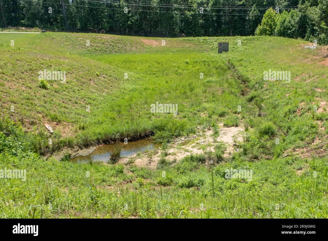 Grande fosso di drenaggio rivestito di erba e erbacce dietro una suddivisione Foto Stock