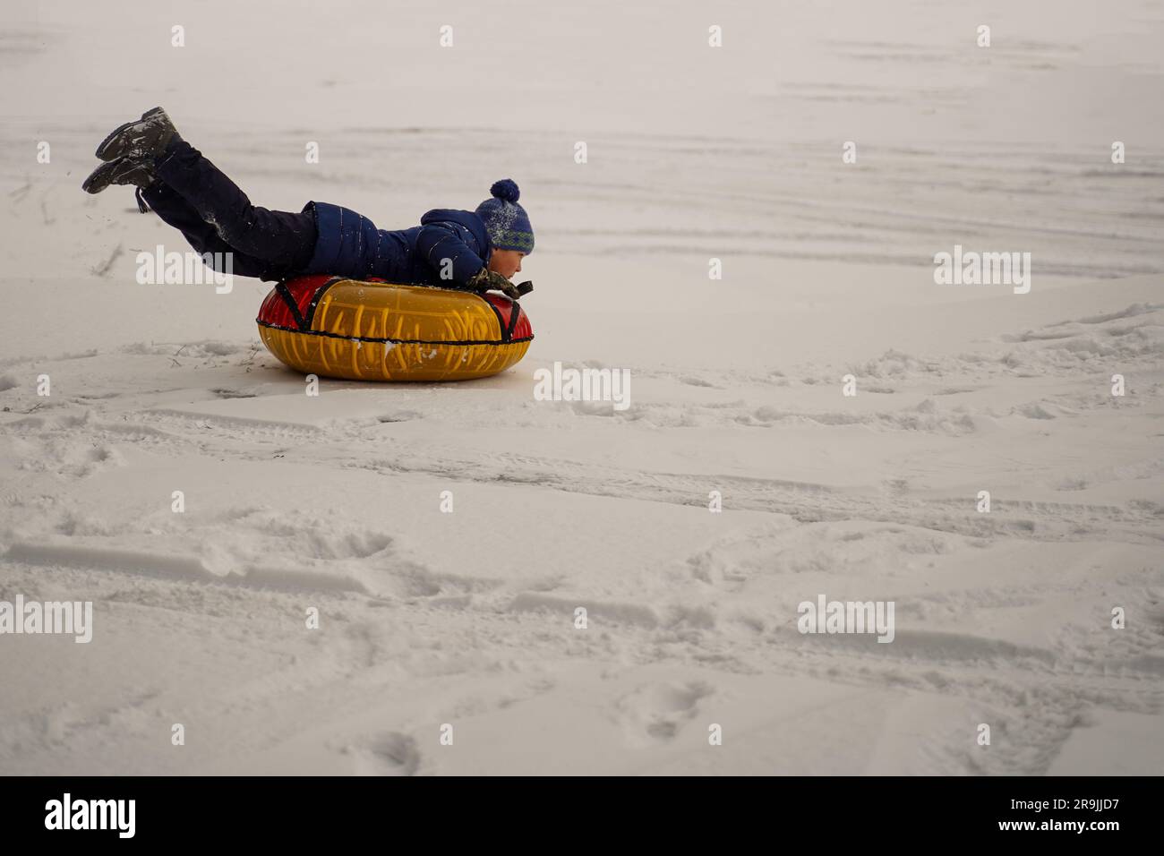 Il ragazzo sta correndo allegramente sul tubing attraverso la pianura innevata. Buone vacanze invernali. Attività sulla neve. Foto Stock