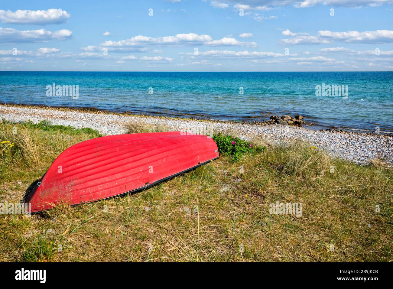 Una barca a remi rossa che giace a testa in giù sulla spiaggia di Skovmose sull'isola danese di ALS. Foto Stock