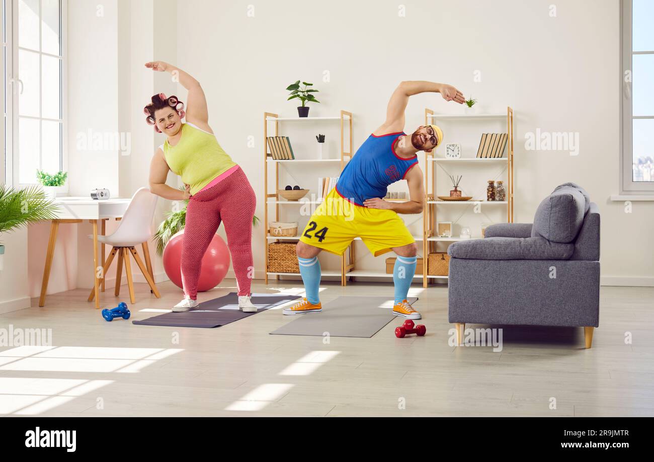 Donna grassa con un uomo barbuto divertente in un brillante abbigliamento sportivo che fa esercizi sportivi a casa insieme. Foto Stock