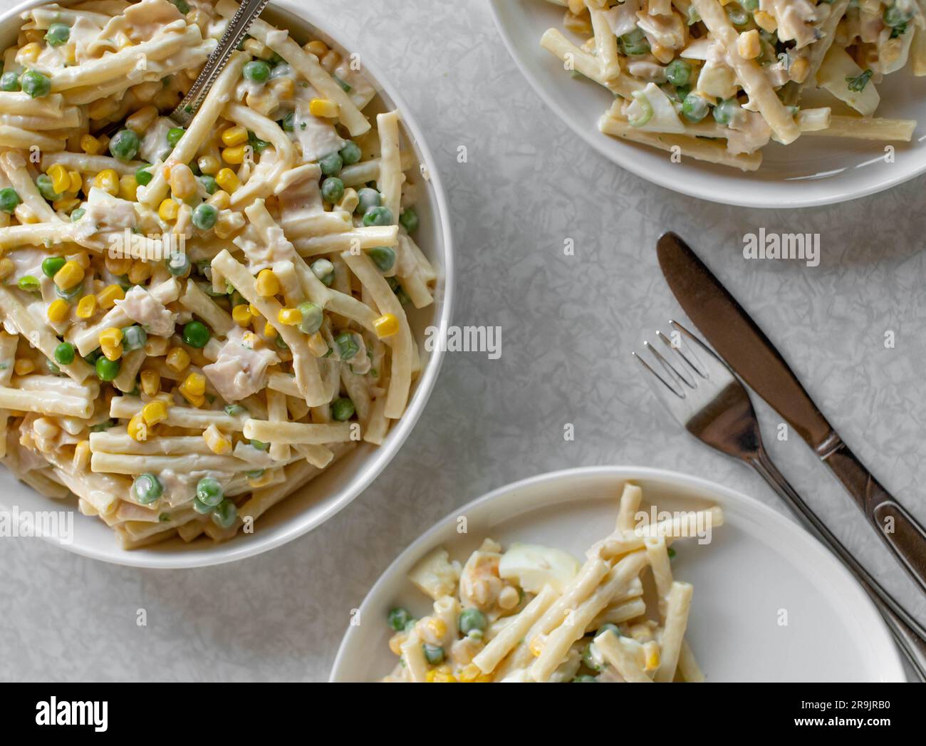 Insalata di pasta classica con maionese, uova sode, mais, piselli verdi, cipolle e salsiccia in un recipiente su sfondo chiaro dall'alto Foto Stock