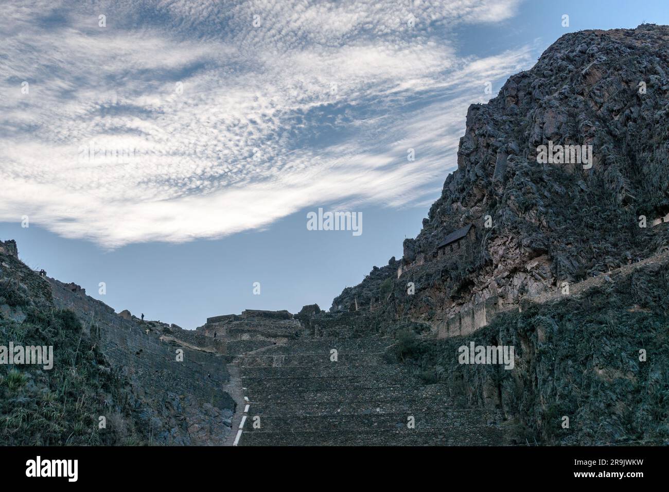 Ollantaytambo, scalini in pietra e terrazze su una ripida parete rocciosa tra le montagne, piccole case e persone sul sentiero. Foto Stock