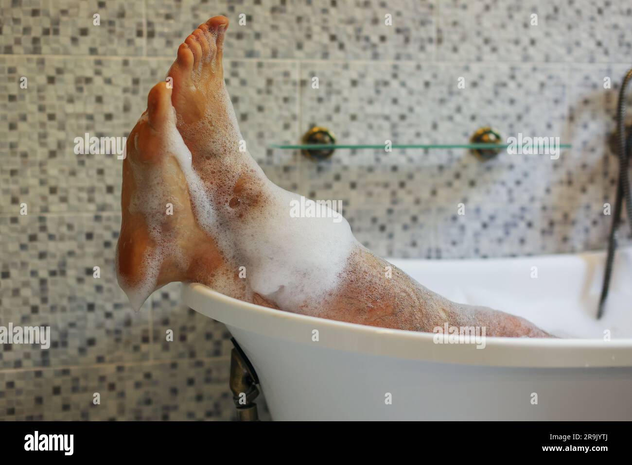 I piedi da uomo sono ricoperti da un bagno di schiuma in una lussuosa vasca da bagno con felicità e relax Foto Stock