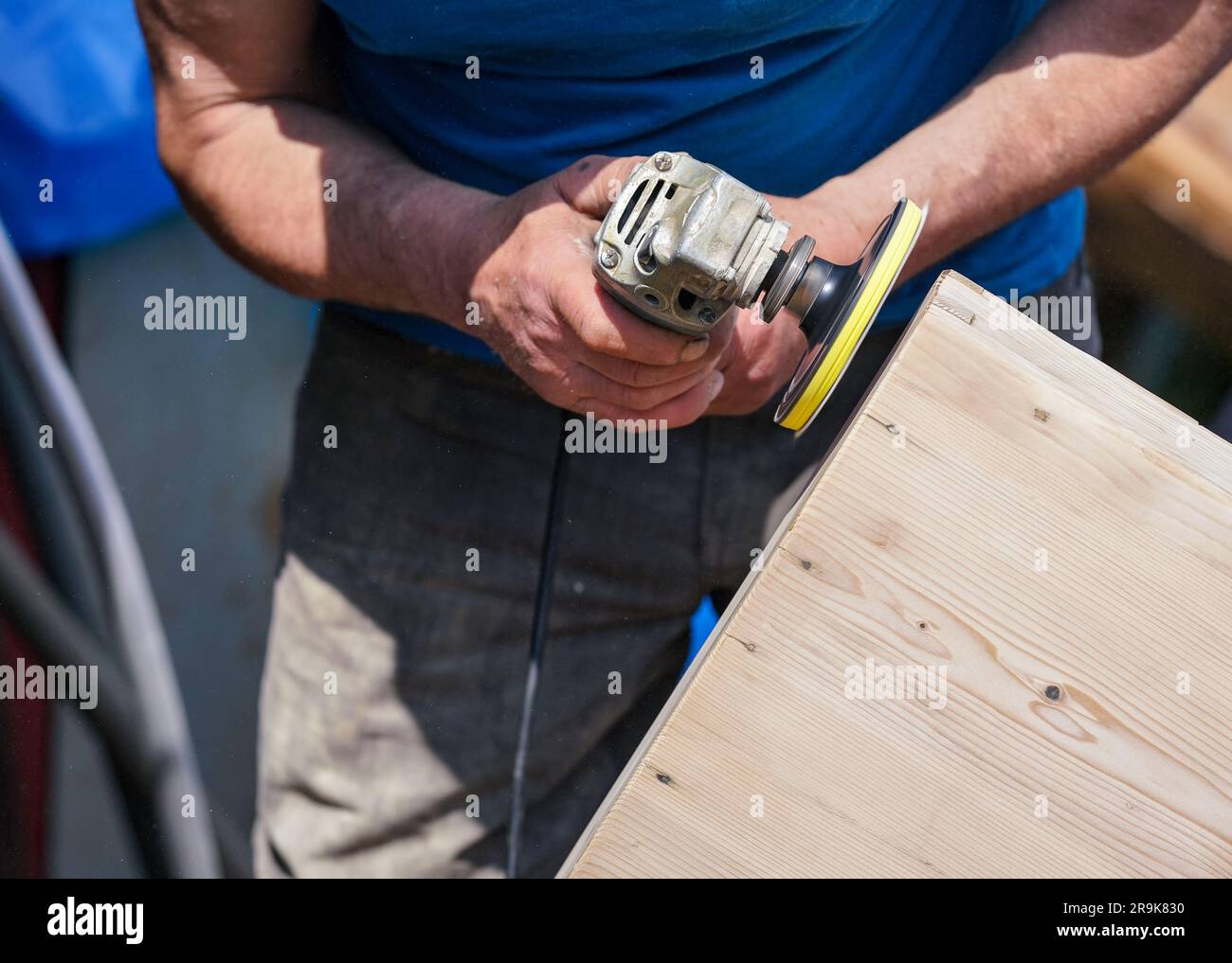 Uomo lucidare il petto di legno con vecchio smerigliatore angolare durante le giornate di sole, primo piano particolare alle mani senza guanti Foto Stock