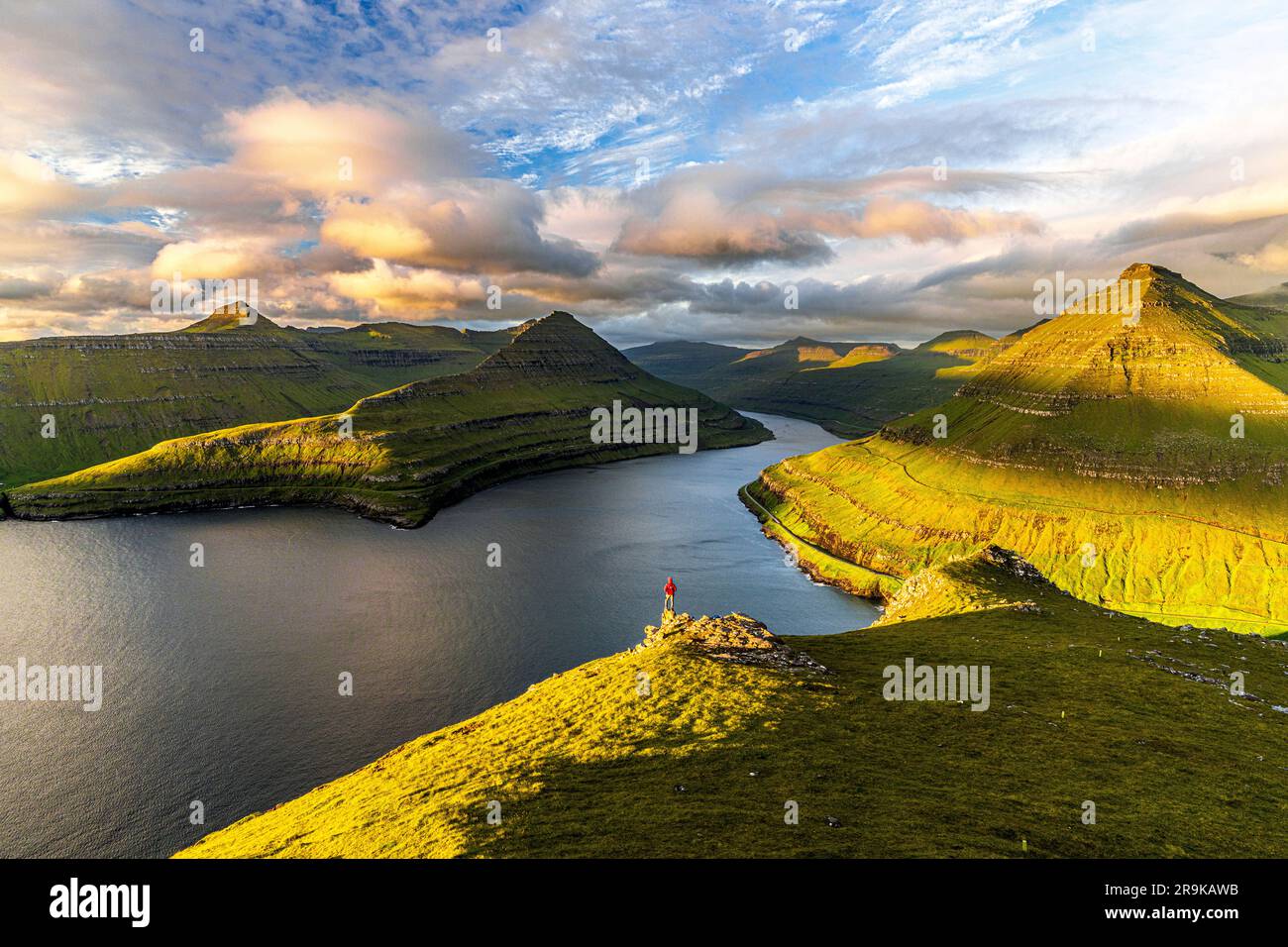 Vista dall'alto dell'escursionista che guarda l'alba sulle scogliere sopra il fiordo di Funningur, l'isola Eysturoy e le isole Faroe Foto Stock
