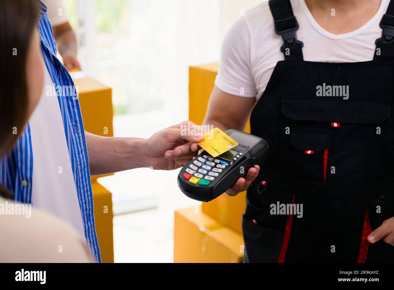 Giovane uomo e donna che paga le scatole di consegna con carta di credito, uomo e donna che accetta e tiene in mano le scatole dei pacchi di consegna dal corriere a casa Foto Stock