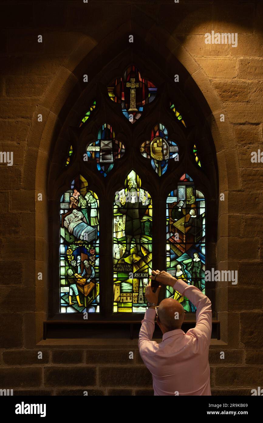 Visitatore che scatta una foto della finestra della peste, Eyam St Lawrences Parish Church, Eyam, Derbyshire, Inghilterra, Regno Unito Foto Stock