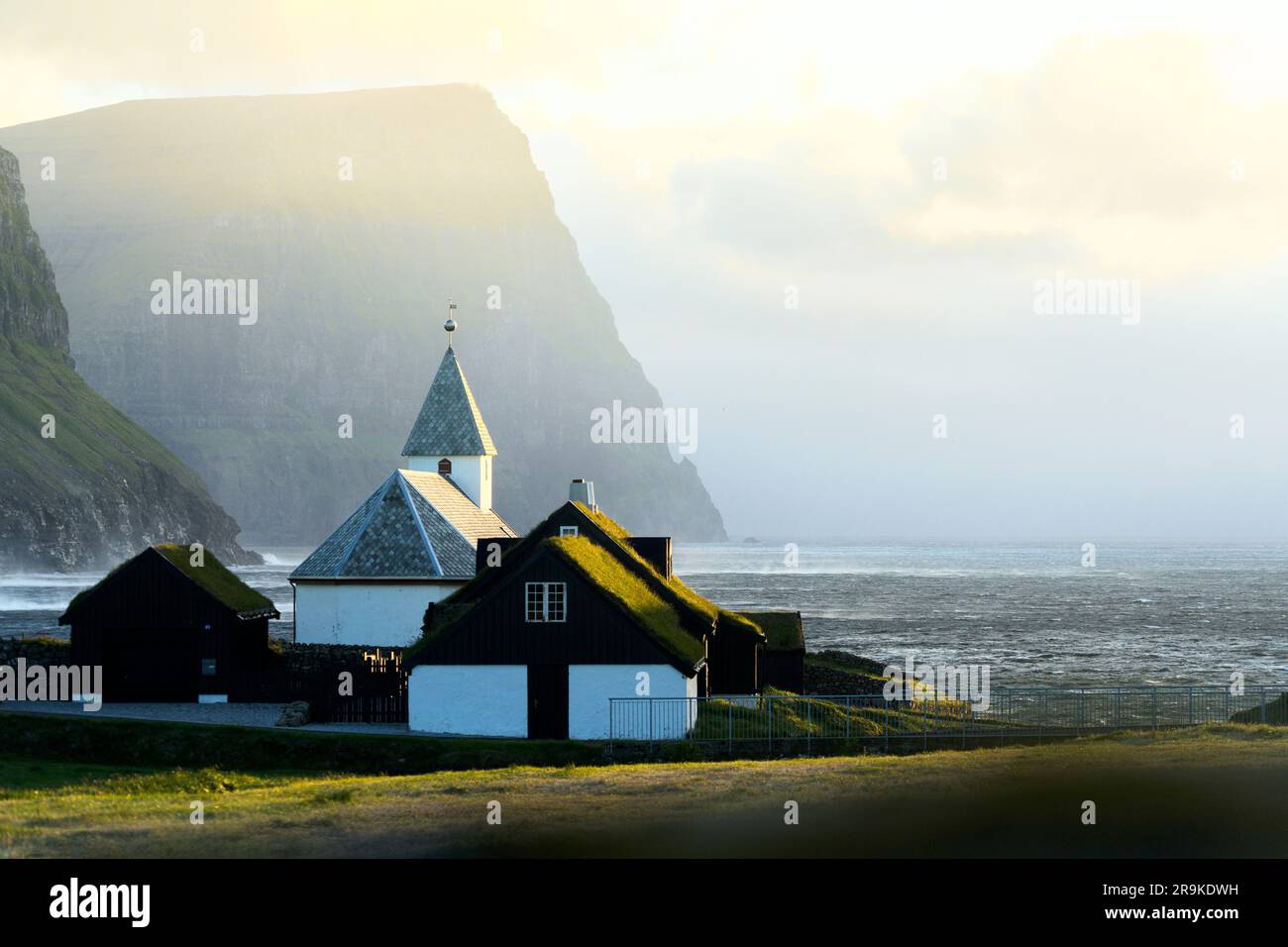 Case sul tetto in erba e vecchia chiesa di Vidareidi sotto la nebbia al tramonto, Vidoy Island, Isole Faroe Foto Stock