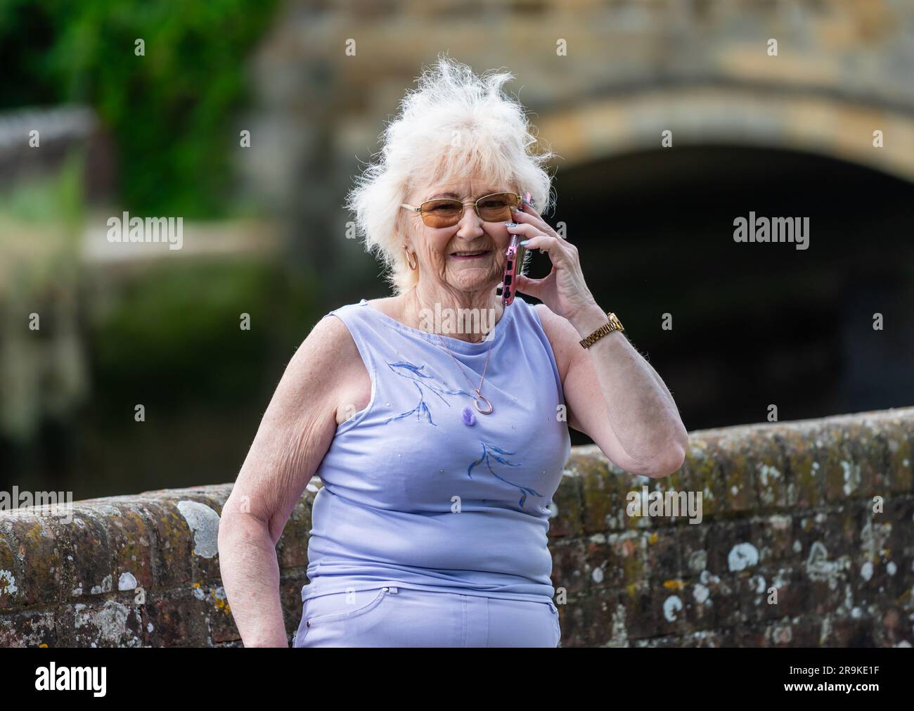 Signora anziana in piedi all'esterno che usa un telefono cellulare, un cellulare o uno smartphone per parlare con qualcuno. Donna anziana aggiornata con la tecnologia moderna, Regno Unito. Foto Stock