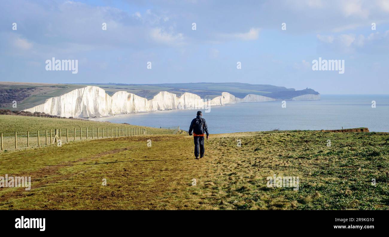 Eastbourne, Regno Unito, 21 gennaio 2023. Vista posteriore di un escursionista di sesso maschile che cammina verso la scogliera Seven Sisters in Inghilterra in una giornata di sole Foto Stock