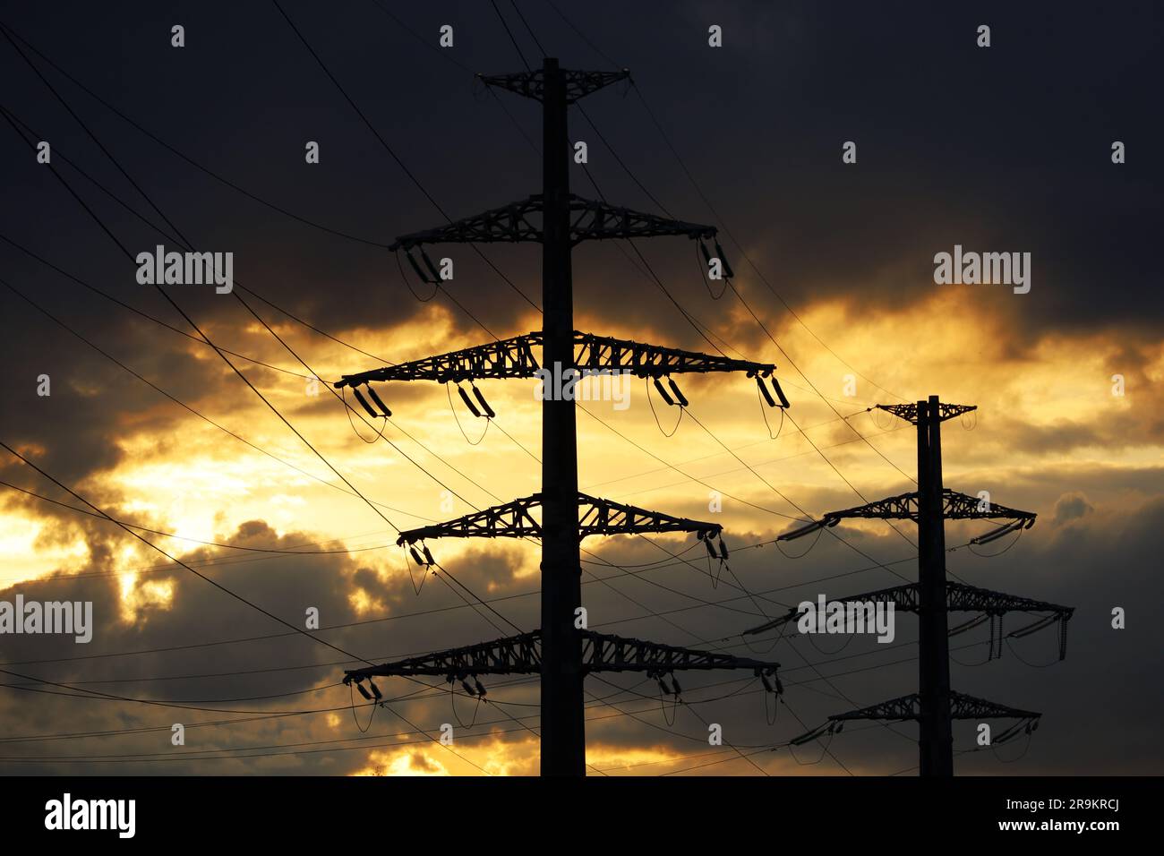 Sagome della torre ad alta tensione con fili elettrici sullo sfondo del cielo del tramonto e nuvole scure. Linee di trasmissione dell'energia elettrica, alimentazione elettrica Foto Stock