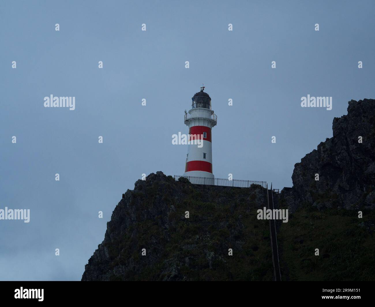 Vista panoramica dell'edificio del faro a strisce rosse e bianche arroccato sulla cima di una collina di scogliera sull'oceano, Cape Palliser Wellington North Island New Zealan Foto Stock