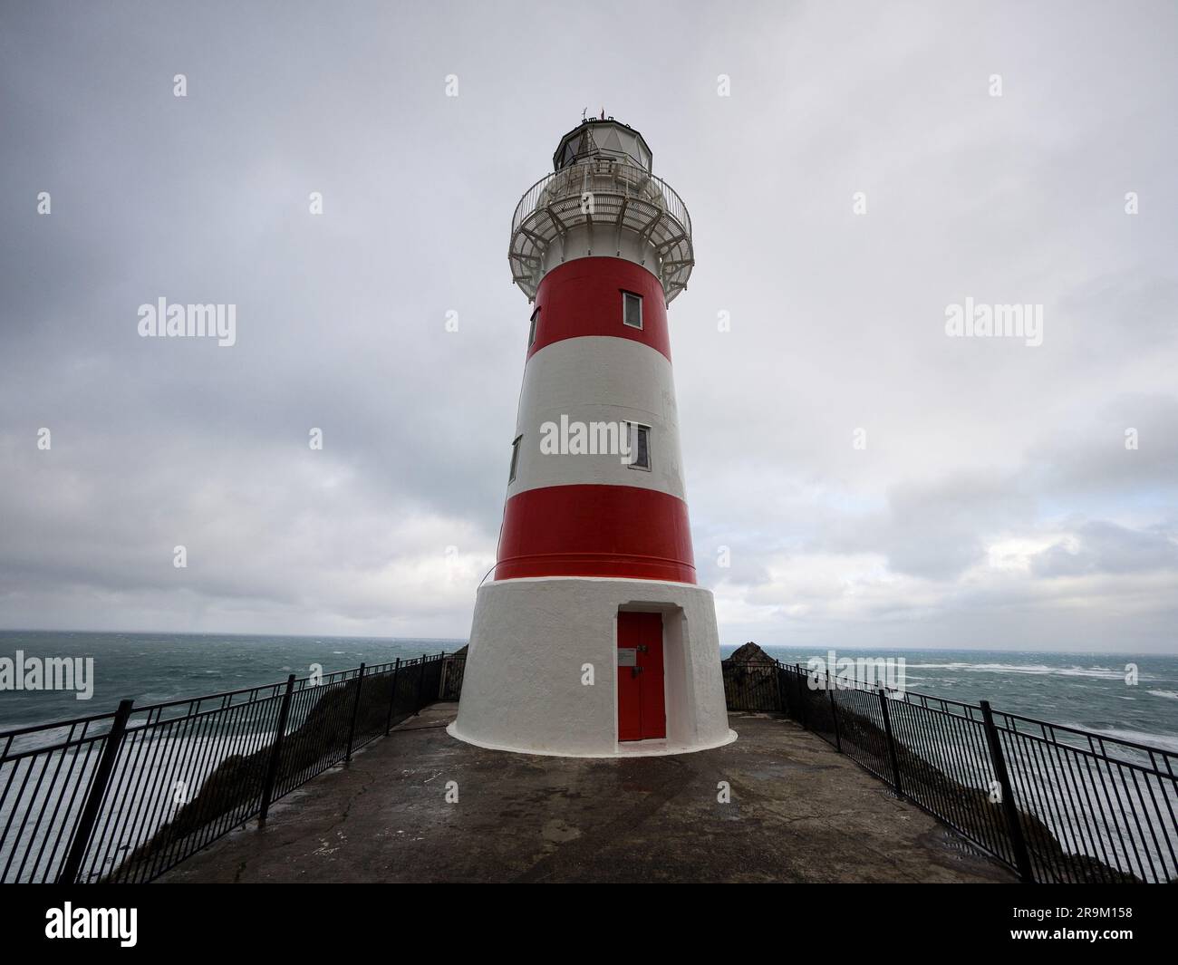 Vista panoramica dell'edificio del faro a strisce rosse e bianche arroccato sulla cima di una collina di scogliera sull'oceano, Cape Palliser Wellington North Island New Zealan Foto Stock