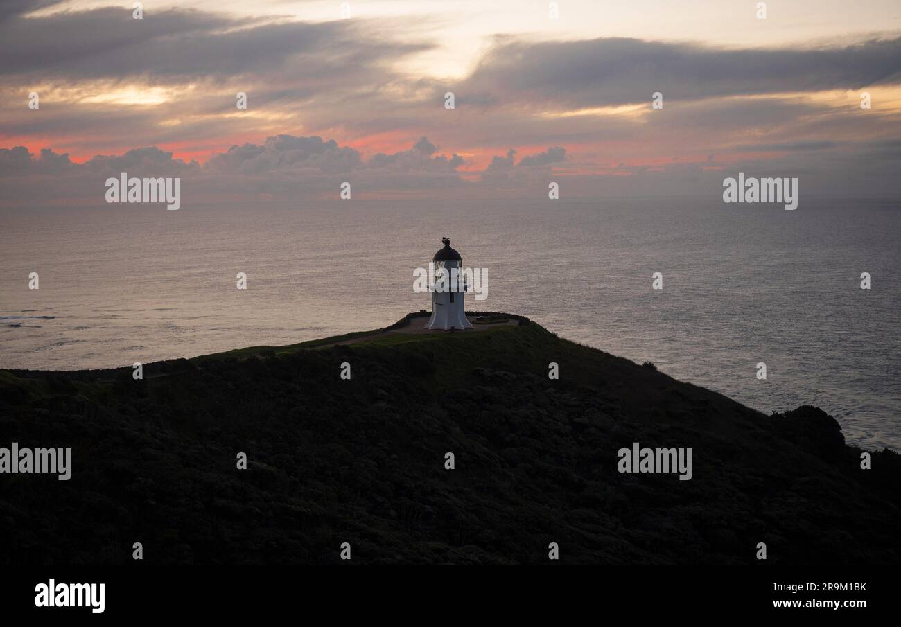 Vista panoramica dello storico faro bianco di Capo Reinga arroccato sulla cima della scogliera sull'oceano durante il tramonto nella penisola di Aupouri nell'Isla settentrionale del Northland Foto Stock