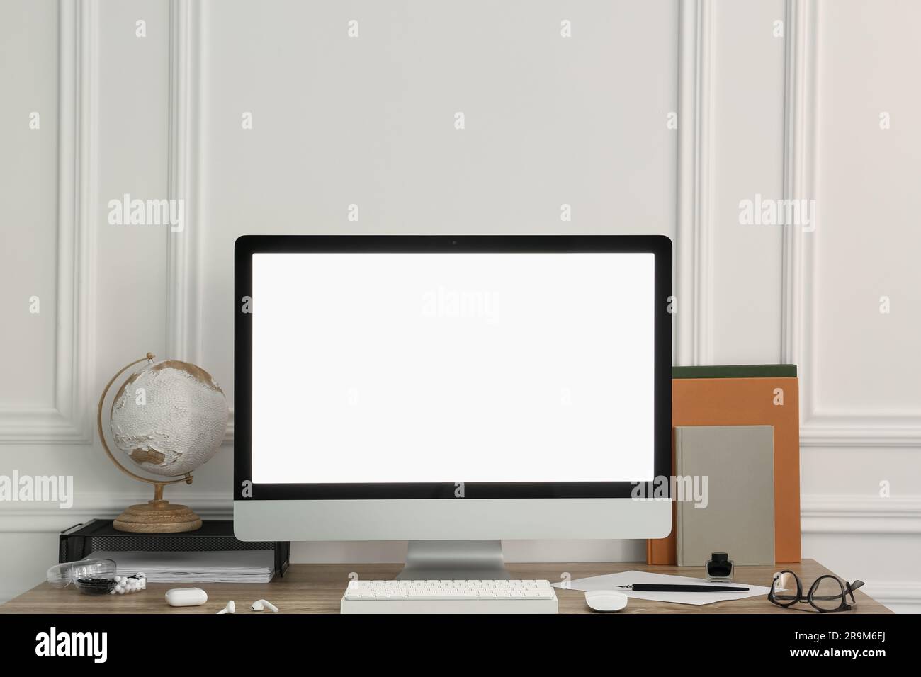 Elegante area di lavoro con computer e cancelleria su una scrivania in legno vicino a una parete bianca Foto Stock