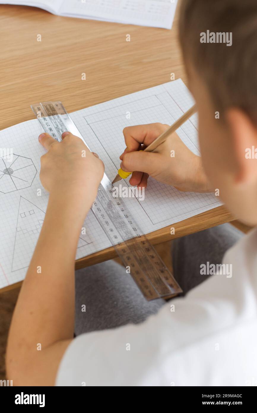 Un ragazzo carino crea un disegno con un righello e una matita. Lezioni a casa. Geometria e disegno. Foto Stock