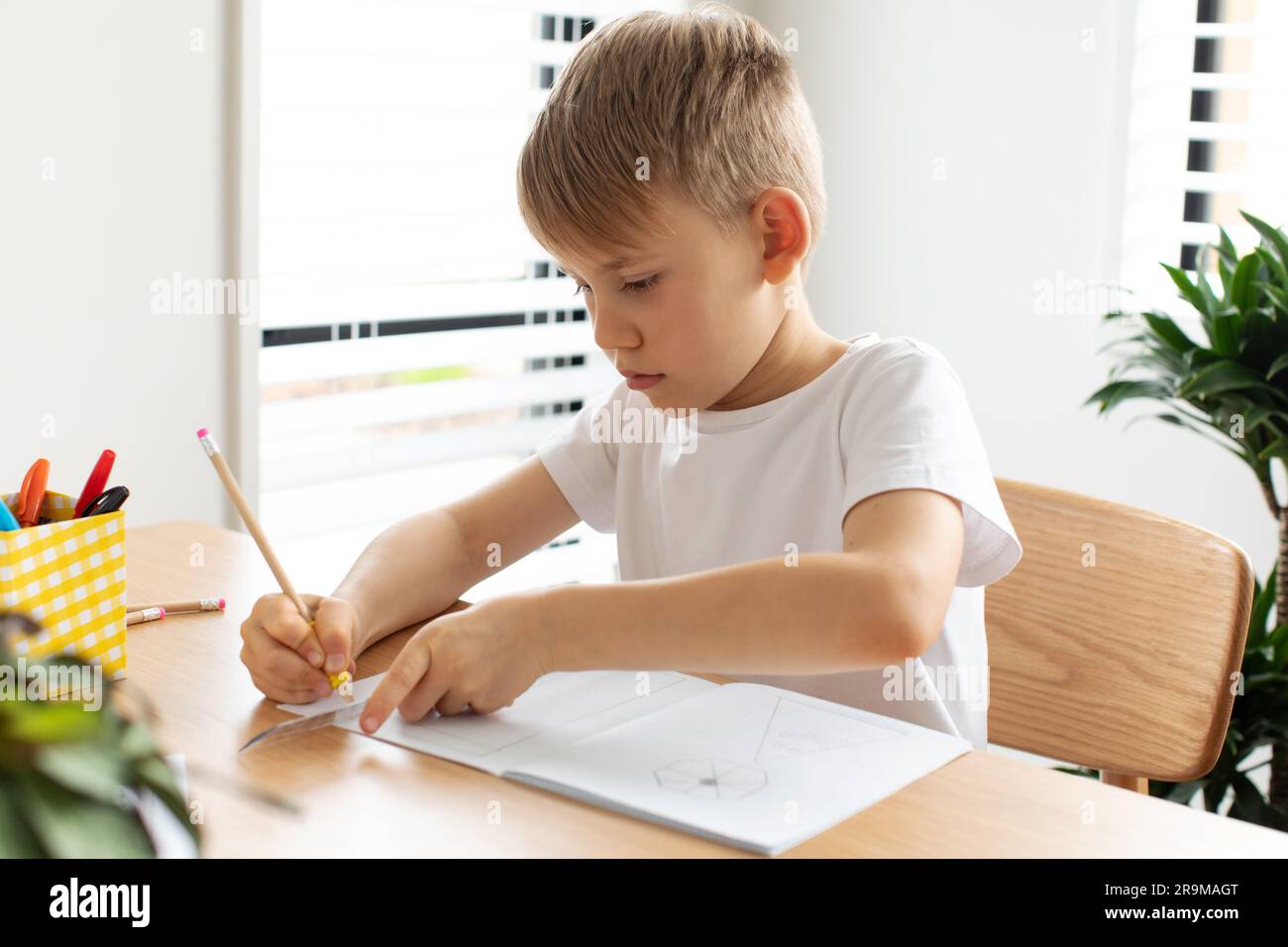 Un ragazzo carino crea un disegno con un righello e una matita. Lezioni a casa. Geometria e disegno. Foto Stock