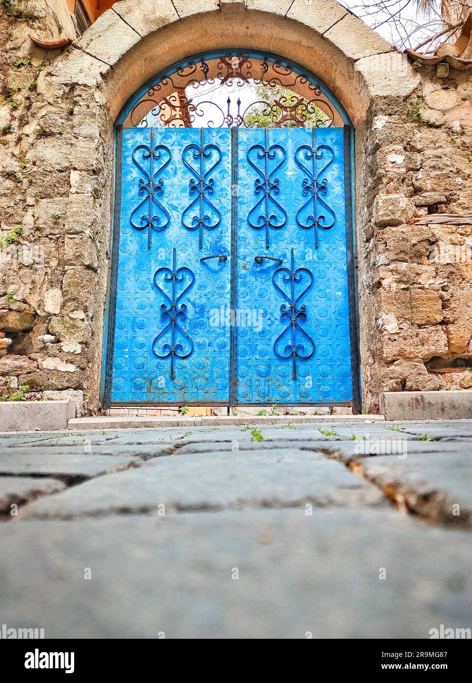 Vecchio cancello blu con forgiatura a motivi sullo sfondo della facciata della vecchia parete in muratura, angolo di visione inferiore Foto Stock