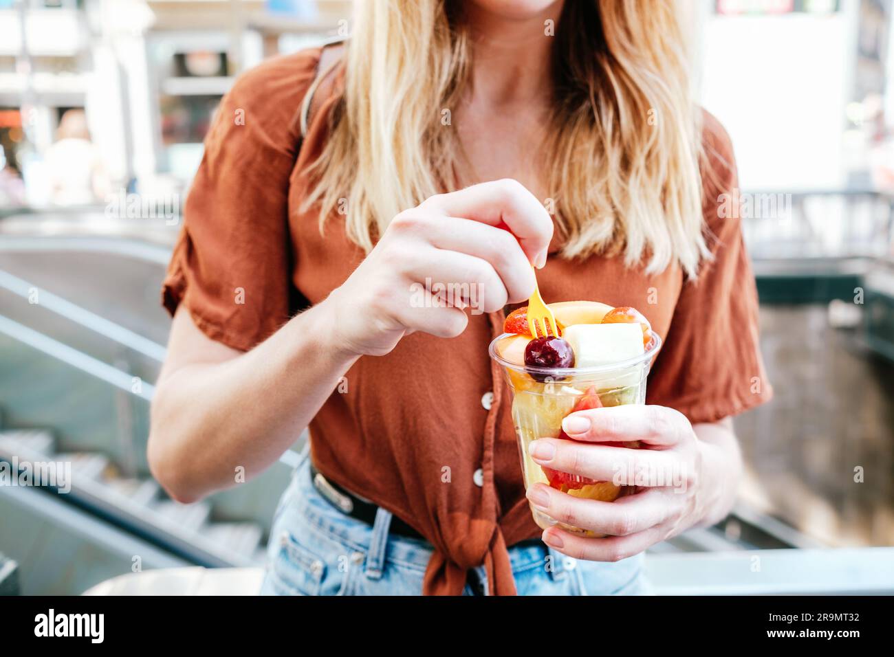 donna bionda irriconoscibile con una tazza di frutta fresca a fette Foto Stock