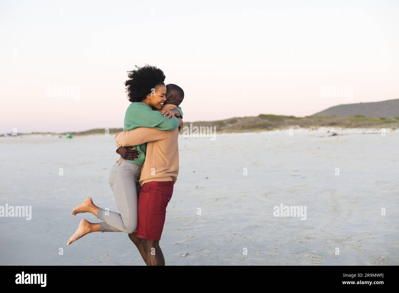 Felice coppia afro-americana che abbraccia e sorride sulla spiaggia al tramonto, spazio fotocopie Foto Stock