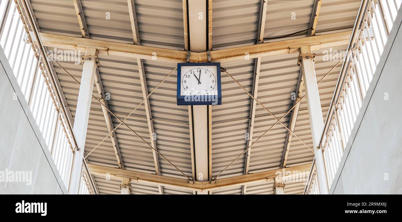 Copertura della stazione ferroviaria in lamiera trapezoidale. Struttura in acciaio. Orologio blu sulla piattaforma Foto Stock