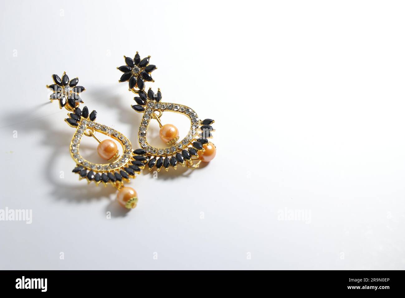 Eleganza irradiata: I gioielli Jumka da donna in oro artificiale brillano su una tela bianca Foto Stock