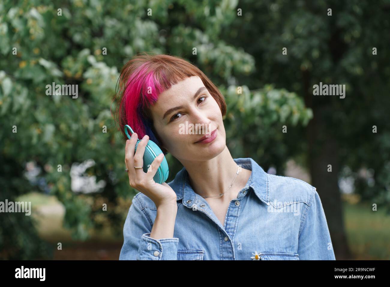 La donna con i capelli rosa ascolta la musica attraverso l'altoparlante musicale portatile nel parco Foto Stock