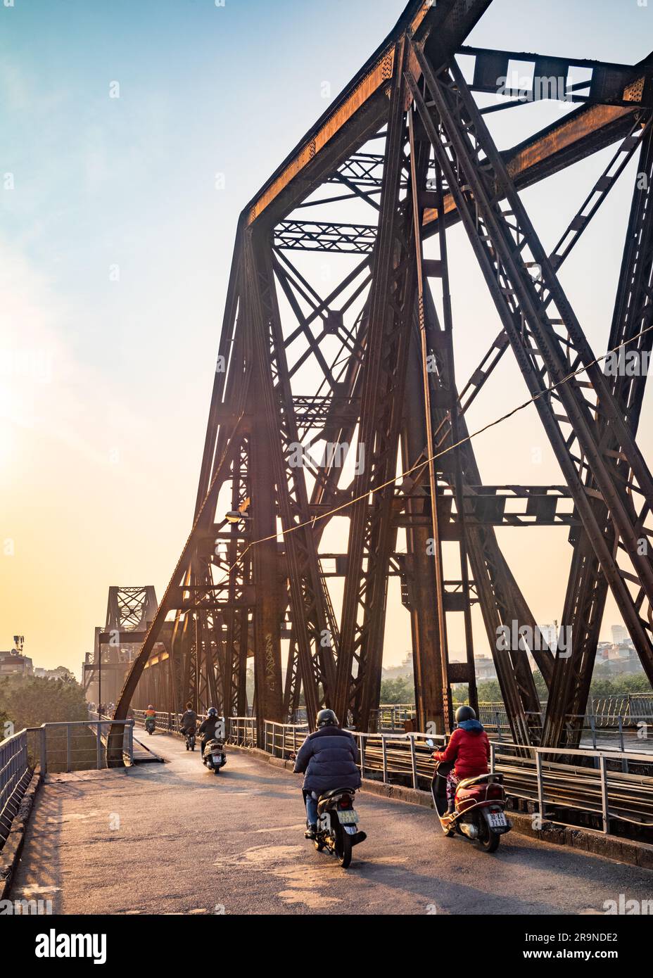 Il traffico motociclistico attraversa la strada condivisa e il ponte ferroviario conosciuto come Long Bien Bridge al crepuscolo ad Hanoi, in Vietnam. Il ponte risale al 1903 e a. Foto Stock