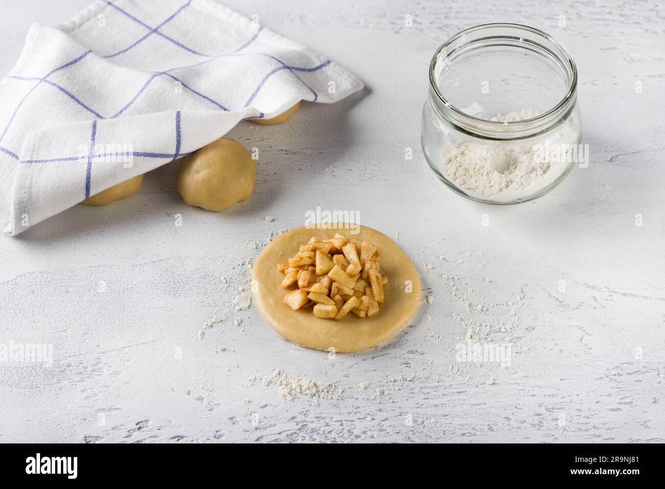 Un pezzo rotondo piatto di pasta arrotolata ripieno di mele e cannella su un tavolo grigio chiaro. Cucinare deliziose mini torte con mele, Foto Stock