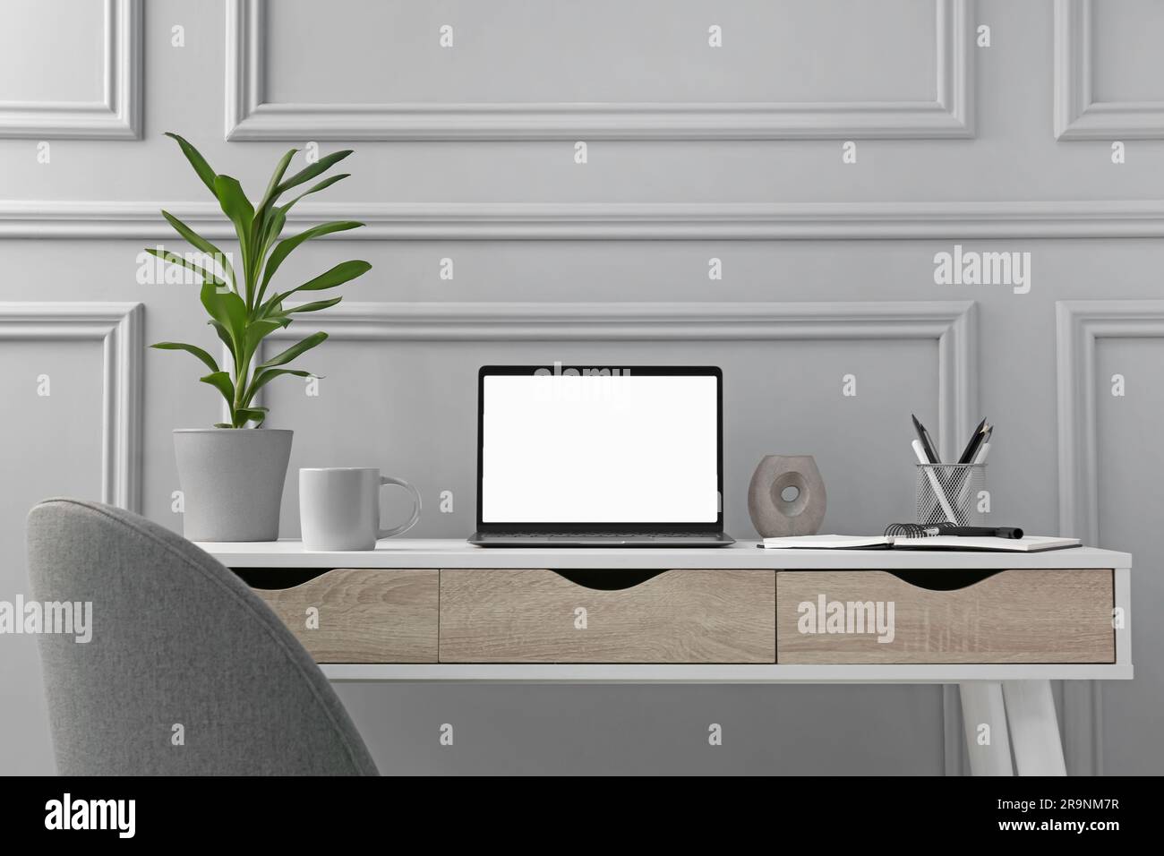 Elegante area di lavoro con computer portatile, cancelleria e piante domestiche su una scrivania in legno Foto Stock