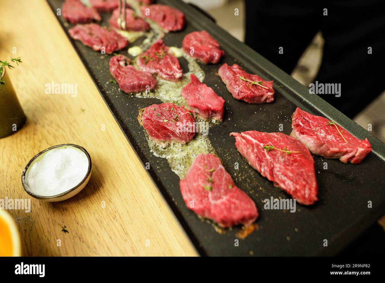 Dettagli poco profondi (messa a fuoco selettiva) con bistecca di manzo cucinata da uno chef su una stufa con burro, sale e rosmarino. Foto Stock