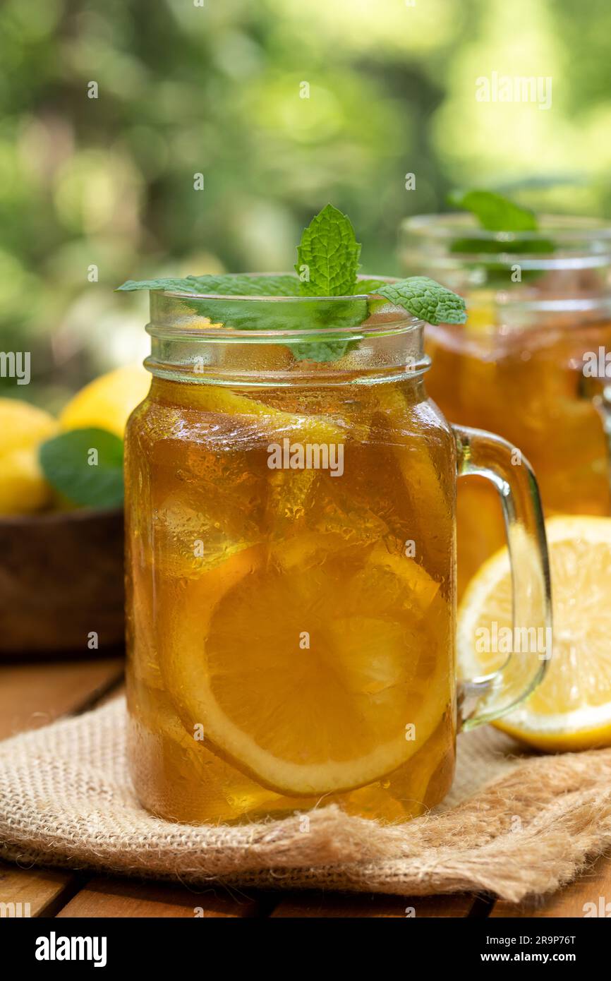 Tè ghiacciato in vasetti di vetro con fettine di limone e menta all'aperto su un tavolo di legno con sfondo naturale Foto Stock