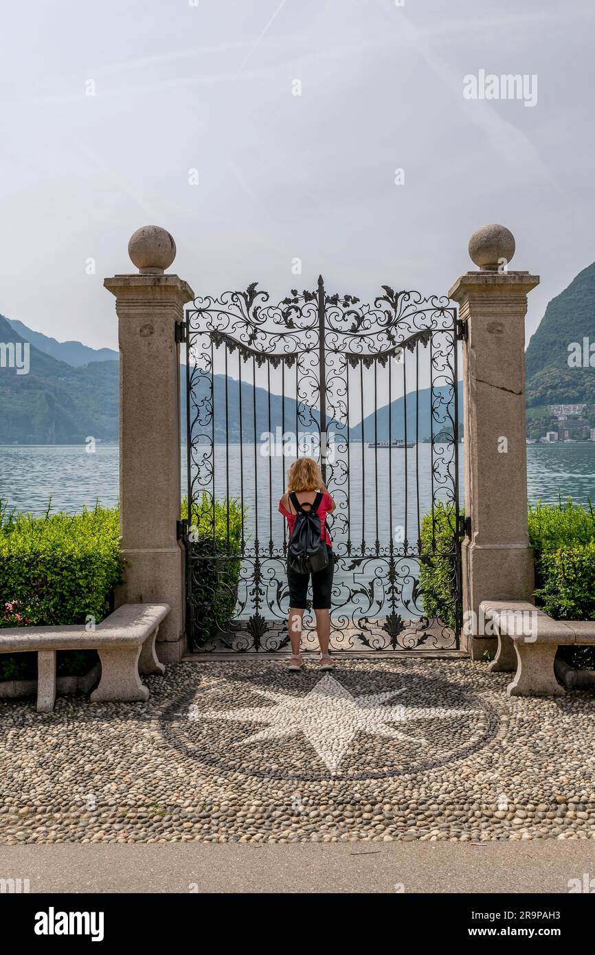 Una donna bionda si affaccia su un cancello di ferro battuto sulla riva del lago di Lugano, in Svizzera Foto Stock